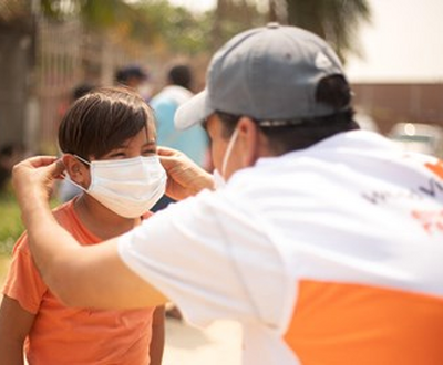 World Vision staff assists a child in Bolivia to wear a mask