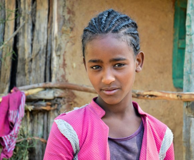 A girl in Ethiopia looks into the camera, wearing a pink jacket