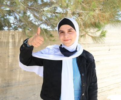 Girl from Gaza wearing a headscarf is looking at the camera and giving a thumbs up.