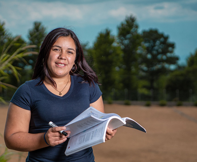 Woman from Honduras flicking between the pages of a book and looking at the camera.