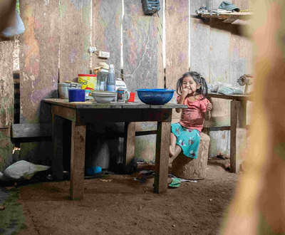 A girl child is siting inside a woode room on a wood stool near the table.