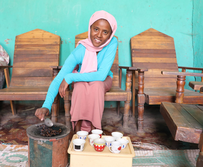 Girl from Ethiopia roasting coffee beans while smiling and looking at the camera