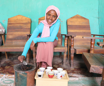 Girl from Ethiopia roasting coffee beans while smiling and looking at the camera 