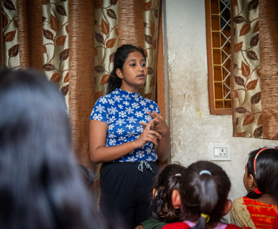 Girl from India educating a group of younger girls about gender violence sat on the floor in front of her.