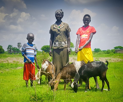 A family in South Sudan smile at the camera and their family goat which will help the family income