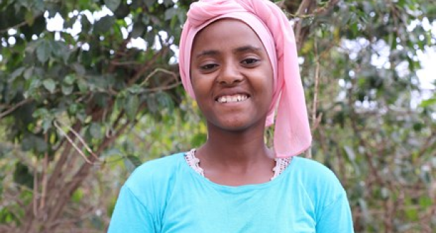 Girl from Ethiopia standing in front of a tree, looking at the camera.