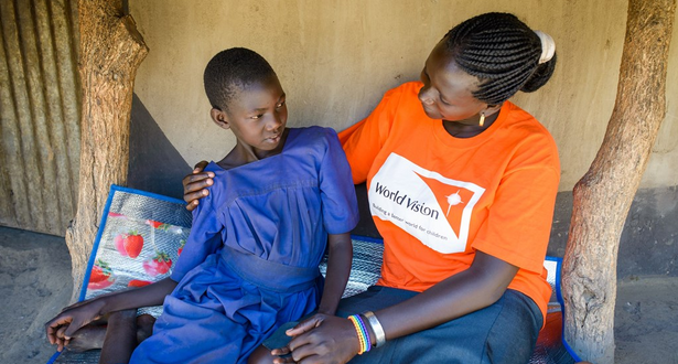 Six World Vision staff in orange tshirts in front of a stand volunteering at a World Vision event