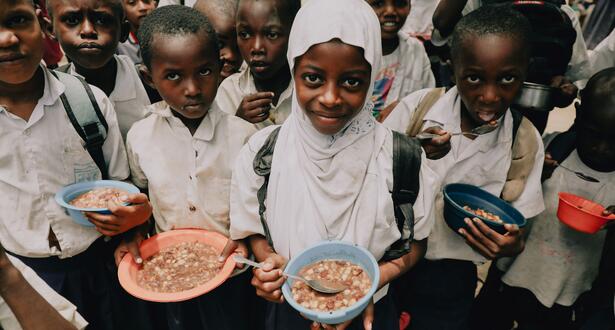 In Tanzania, 9-year-old Rukia (white hijab) holds a plate of food in front of the camera, while her classmates do the same.