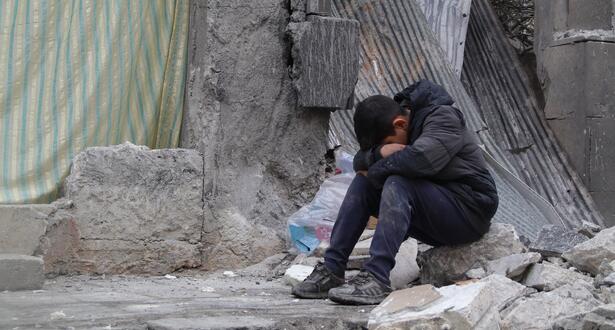 A child sitting amidst a collapsed neighbourhood in Aleppo