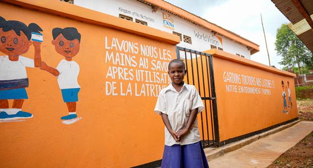 Iragi, 9, poses in front of the toilets built at his school in the DRC