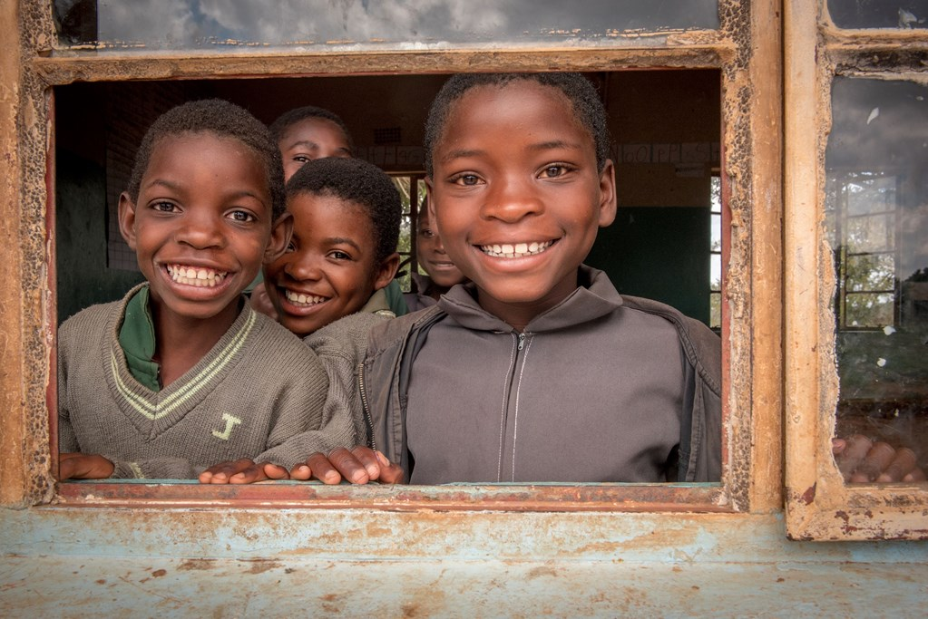 School children peering out of a window, smiling 