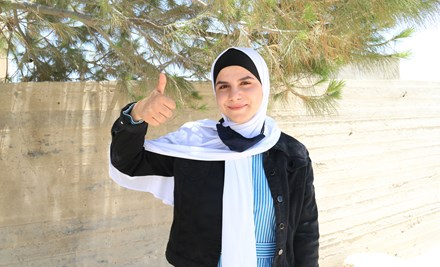 Girl from Gaza wearing a headscarf is looking at the camera and giving a thumbs up.