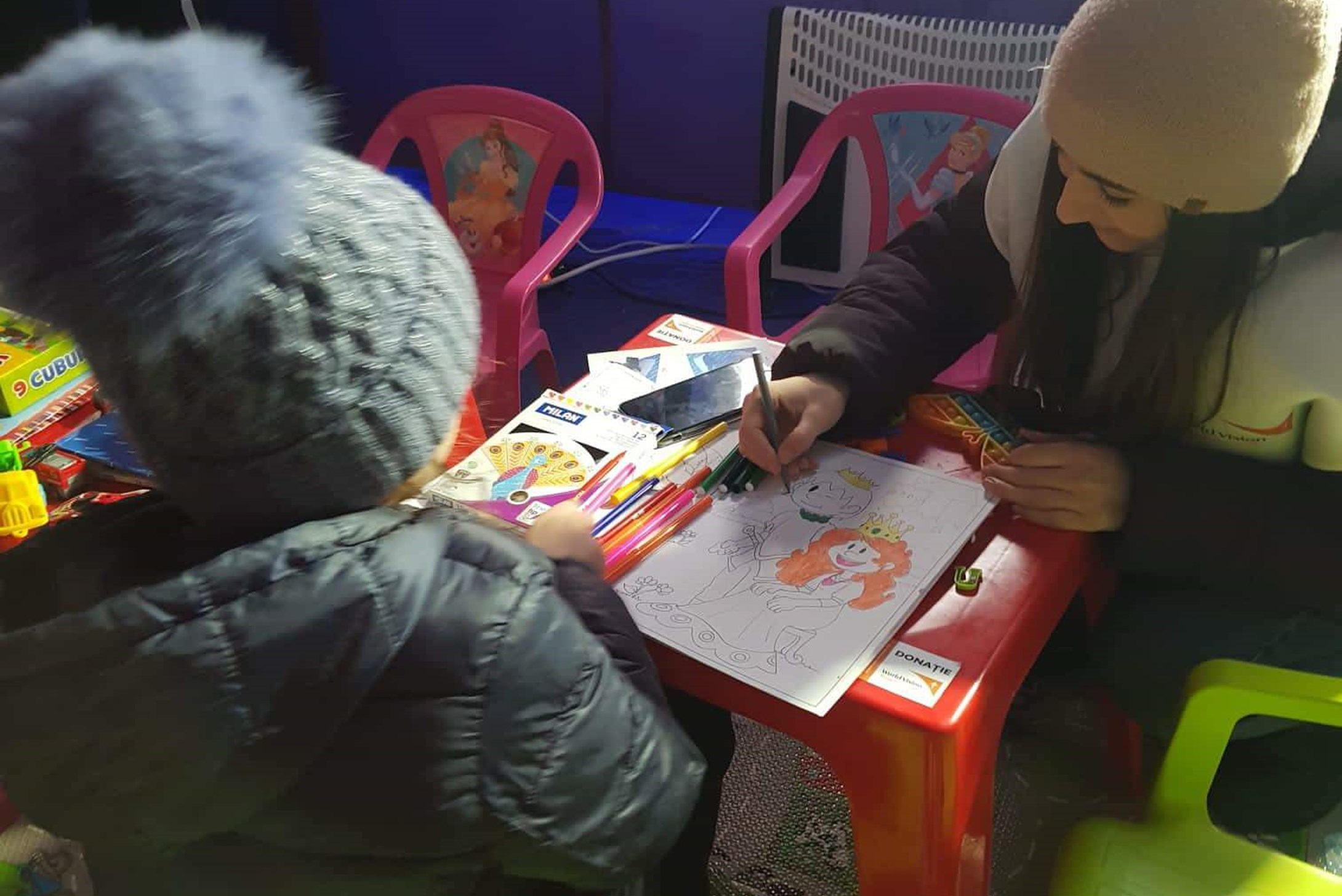 Woman painting with a girl at a camp.