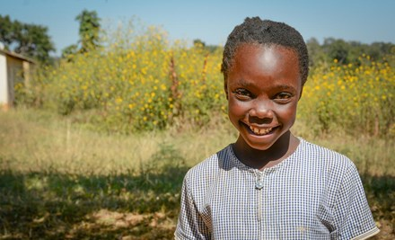 Former sponsored child smiles in field in Zambia