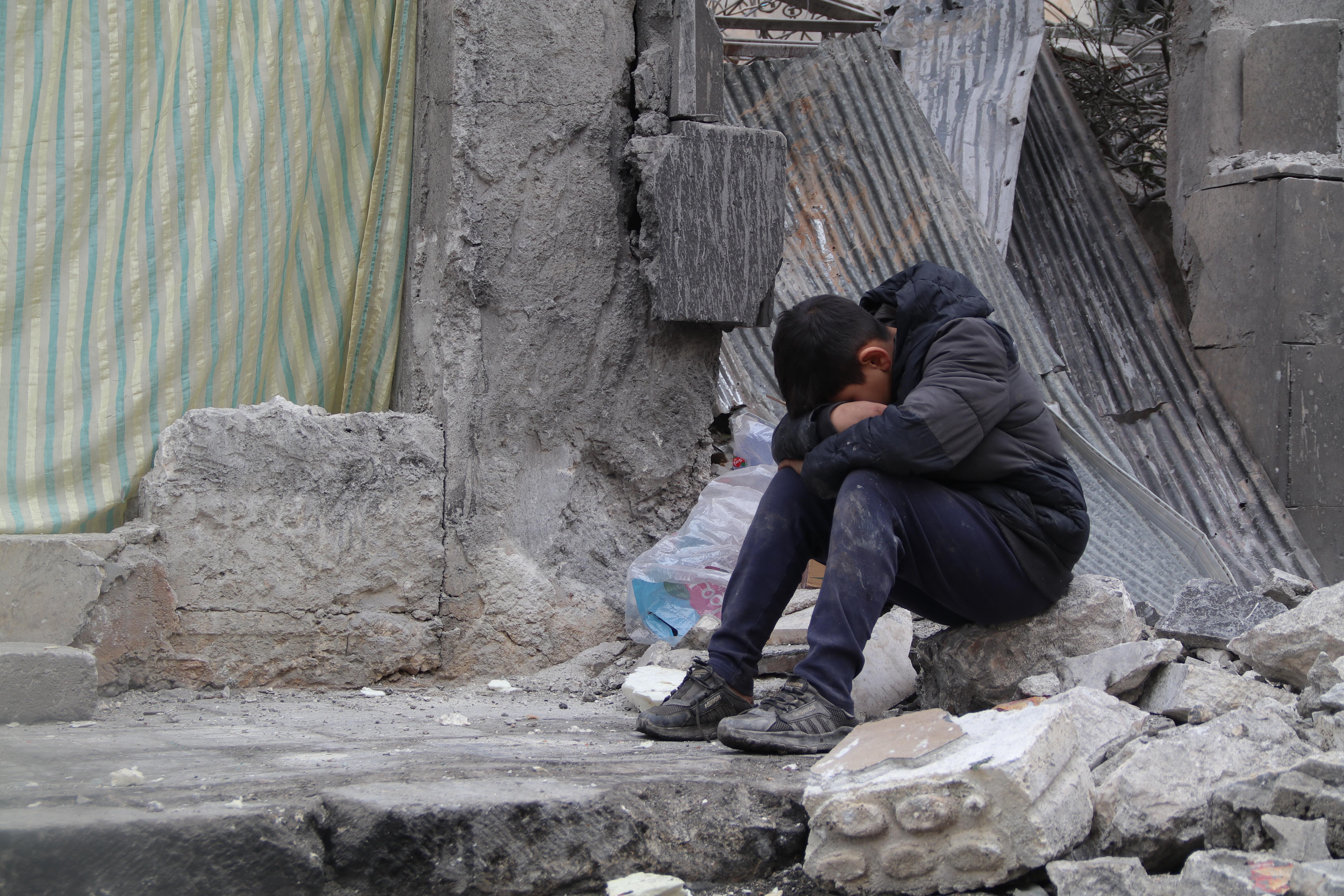 A child sitting amidst a collapsed neighbourhood in Aleppo